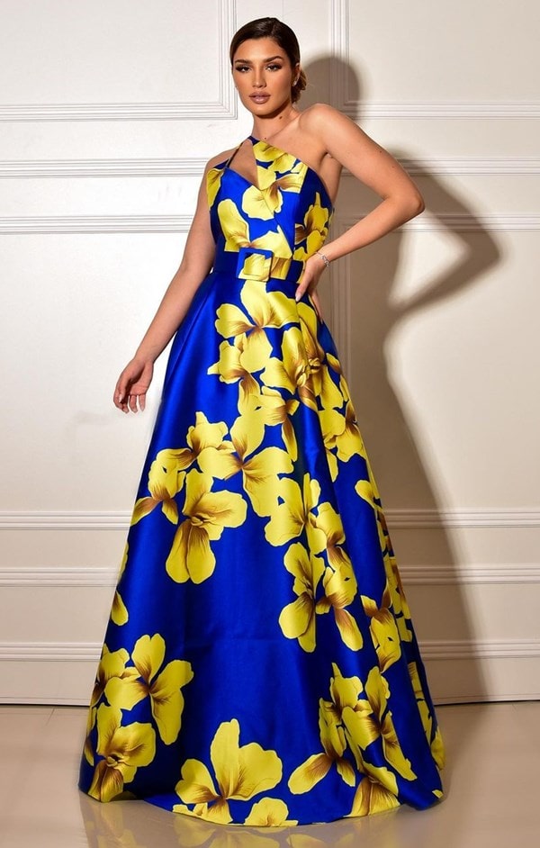 vestido de festa estampado longo azul bic om estampa de maxi flores amarelas. O vestido é de zibeline e possui cinto do mesmo tecido do vestido e decote assimétrico. 