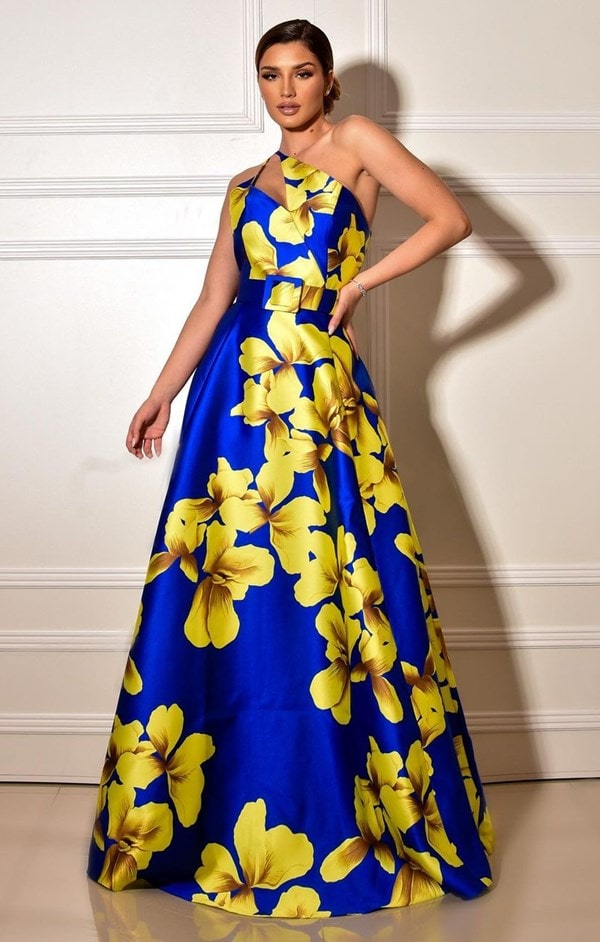 vestido de festa estampado longo azul bic om estampa de maxi flores amarelas. O vestido é de zibeline e possui cinto do mesmo tecido do vestido e decote assimétrico.