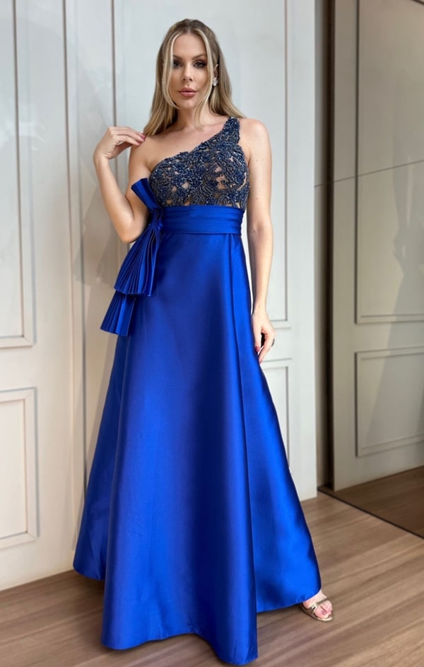 vestido de festa longo azul royal com a saia lisa e corpete bordado em pedrarias. O vestido possui um ombro só.