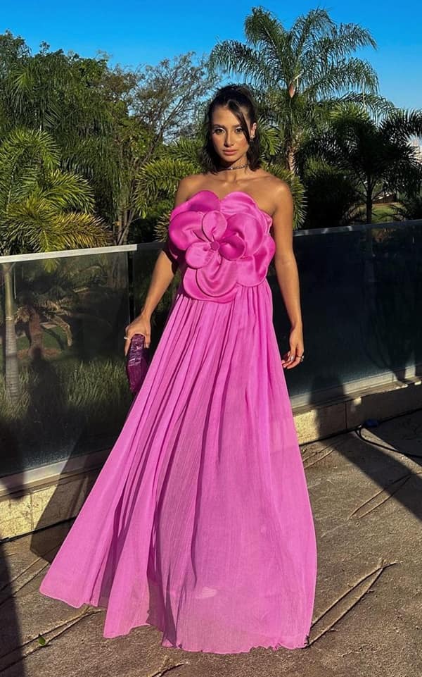 convidada de casamento durante o dia ao ar livre usa vestido de festa longo rosa fluido com  maxi flor na frente do vestido