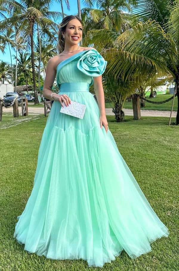 madrinha de casamento durante 
 o dia usando vestido de festa longo verde menta de tule modelo um ombro só com cintura marcada e maxi flor 3D no ombro