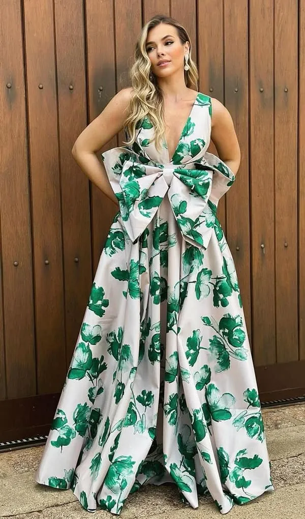 vestido de festa longo branco com estampa de flores verde. O vestido possui maxi laço na frente do vestido